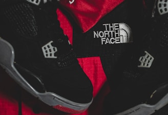Black athletic shoes are placed alongside red and black sportswear bearing logos from Spalding and The North Face.