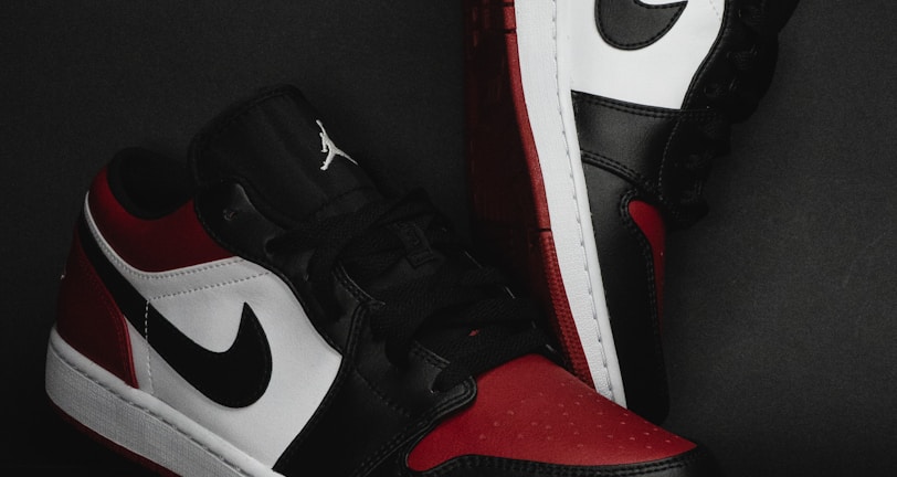 A pair of stylish athletic shoes in black, white, and red colors with distinctive branding. The shoes are positioned against a dark background, showcasing their sleek design and detailed craftsmanship.